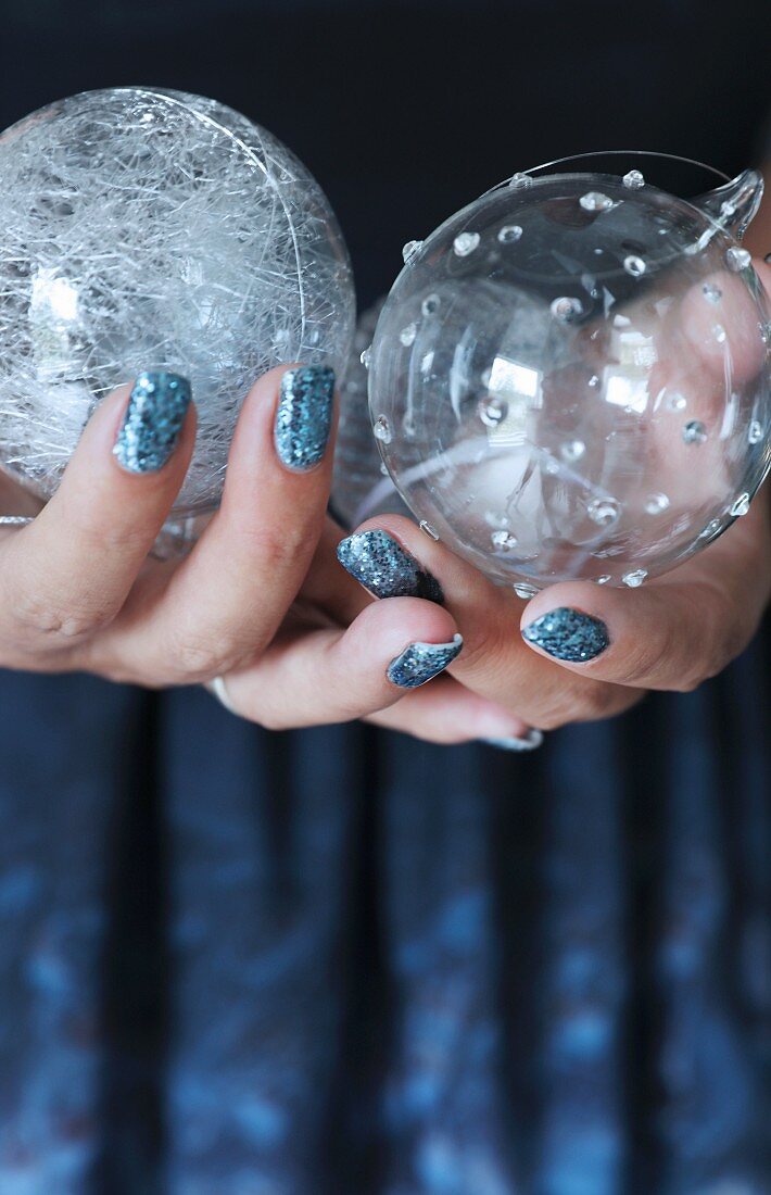 Hände mit glitzernd lackierten Nägeln halten Weihnachtskugeln aus Glas