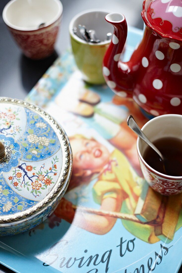 Coffee crockery and a painted porcelain sugar pot on a tray with a retro picture