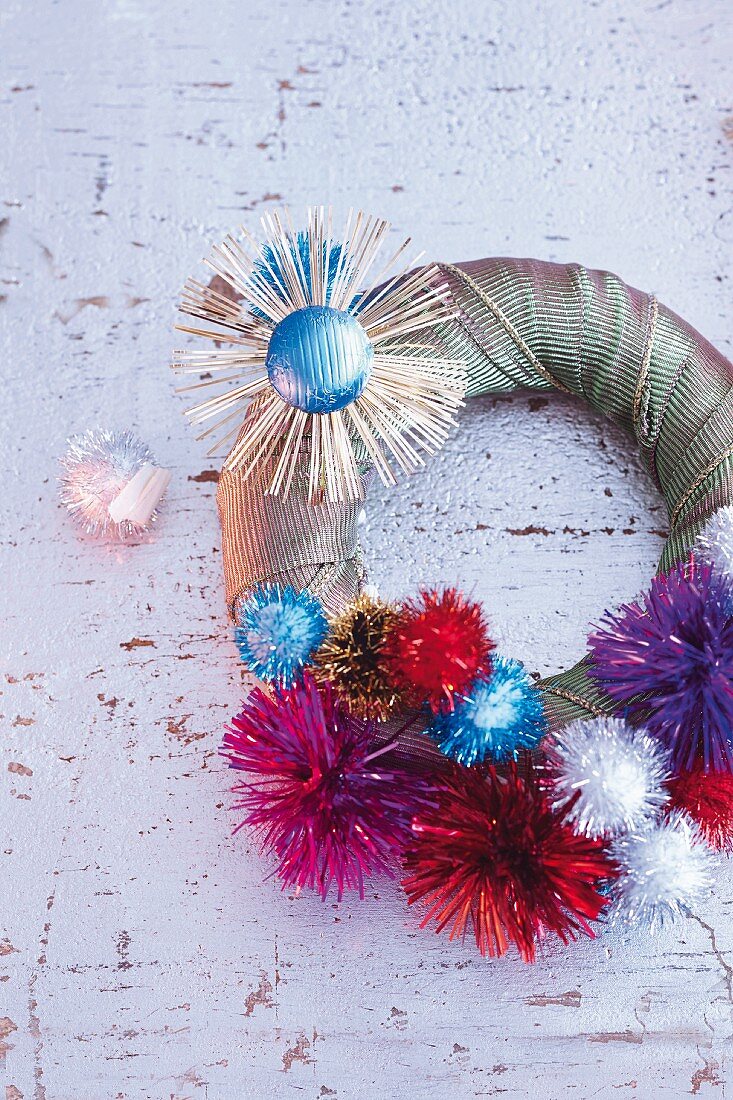 A wreath being decorated with chocolate suns and glittery pompoms