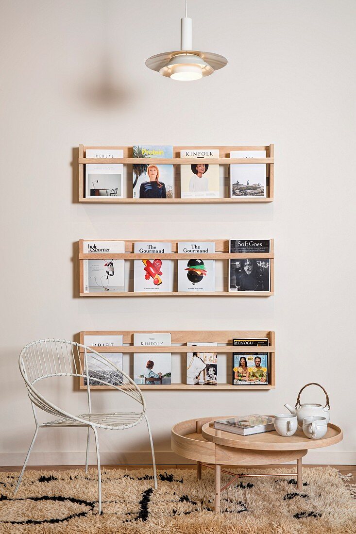 Weißer Retro Metallstuhl und rundes Bodentischchen mit schwenkbarem Tablett aus Holz vor ausgestellten Büchern auf Wandboards
