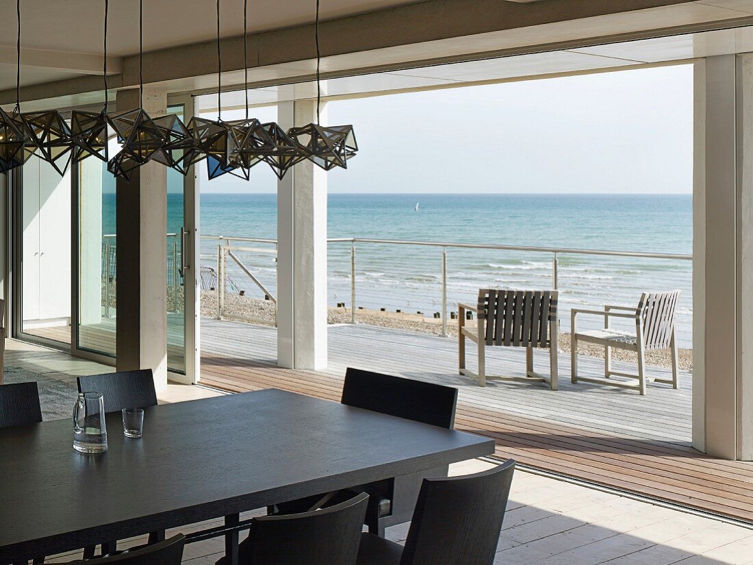 Blick über dunklen Esstisch mit passenden Stühlen auf Terrasse und offenes Meer