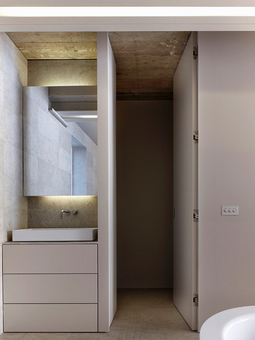 In Nische eingebauter Waschtisch mit Schubladenunterschrank und Spiegel mit indirekter Beleuchtung, offene Tür zum WC-Bereich