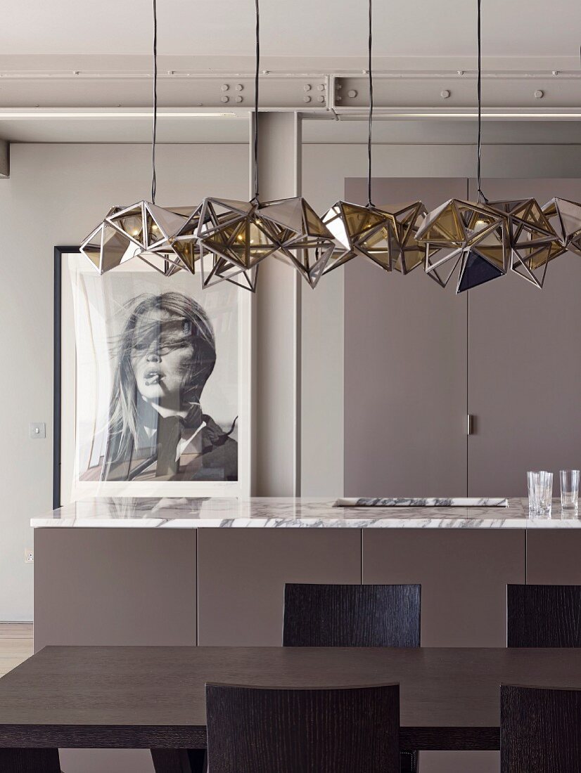 Designer Pendelleuchte über schwarzbraunem Esstisch und Küchentheke mit Marmorarbeitsplatte vor gerahmtem Frauenportraitfoto