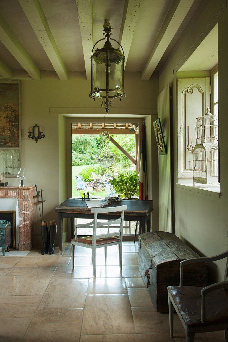 Simple writing desk and armchair in front of terrace doors: old wooden trunk in foreground