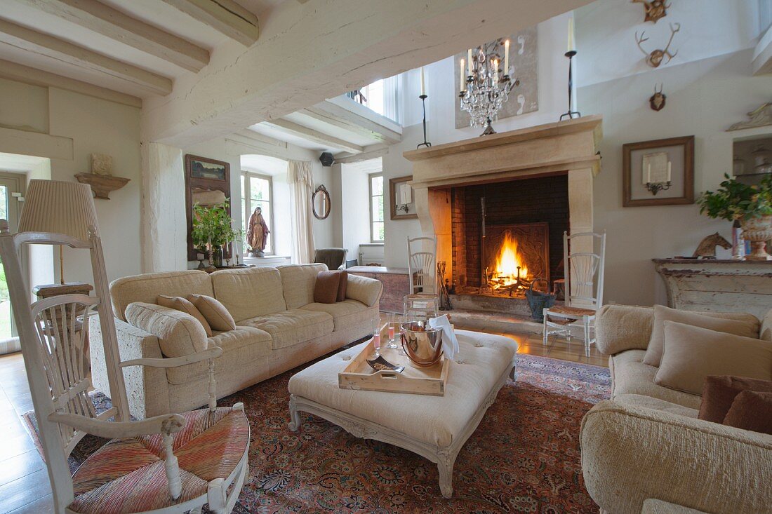 Pale sofa set and ottoman in front of fire in large fireplace in grand country house