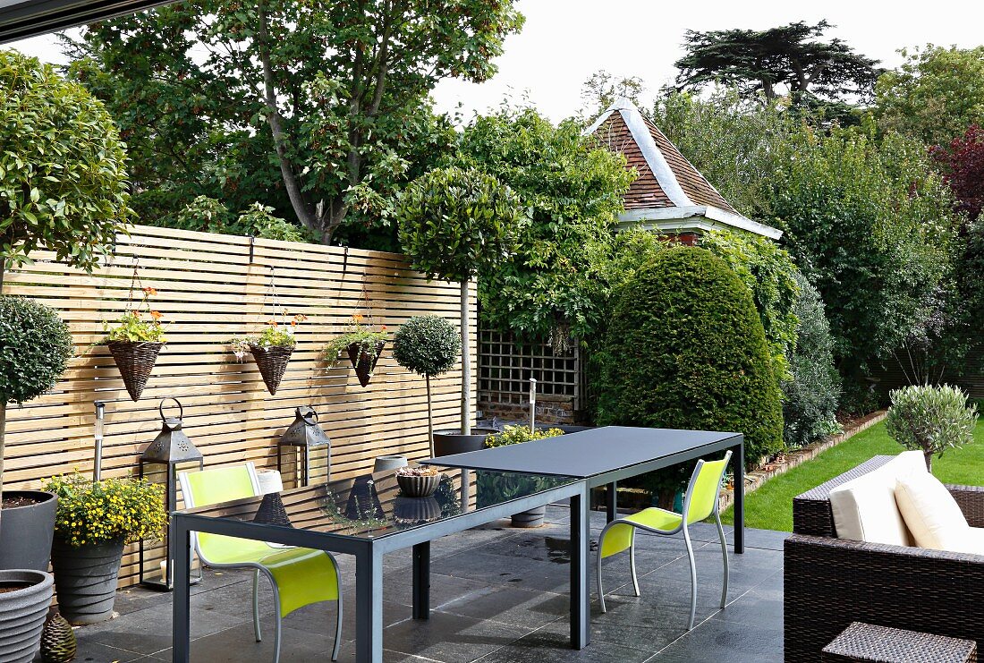 Graue, elegante Outdoortische und neongrüne Stühle auf Terrasse vor Holzlamellen Sichtschutzwand