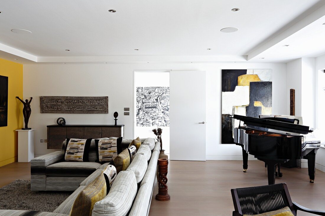 Moderner Wohnraum mit Sofakombination und Klavier vor modernem Bild