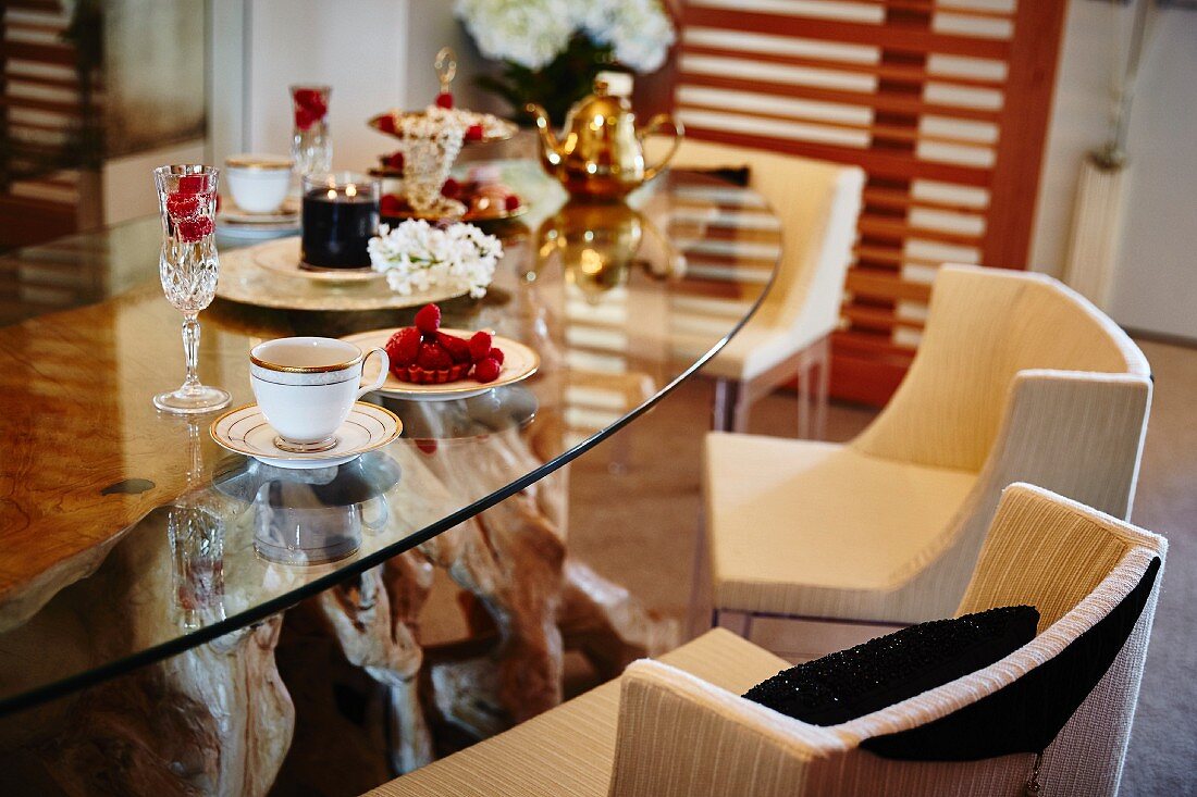 Kaffeegeschirr, Törtchen und Sektglas auf Glastisch, gepolsterte Stühle