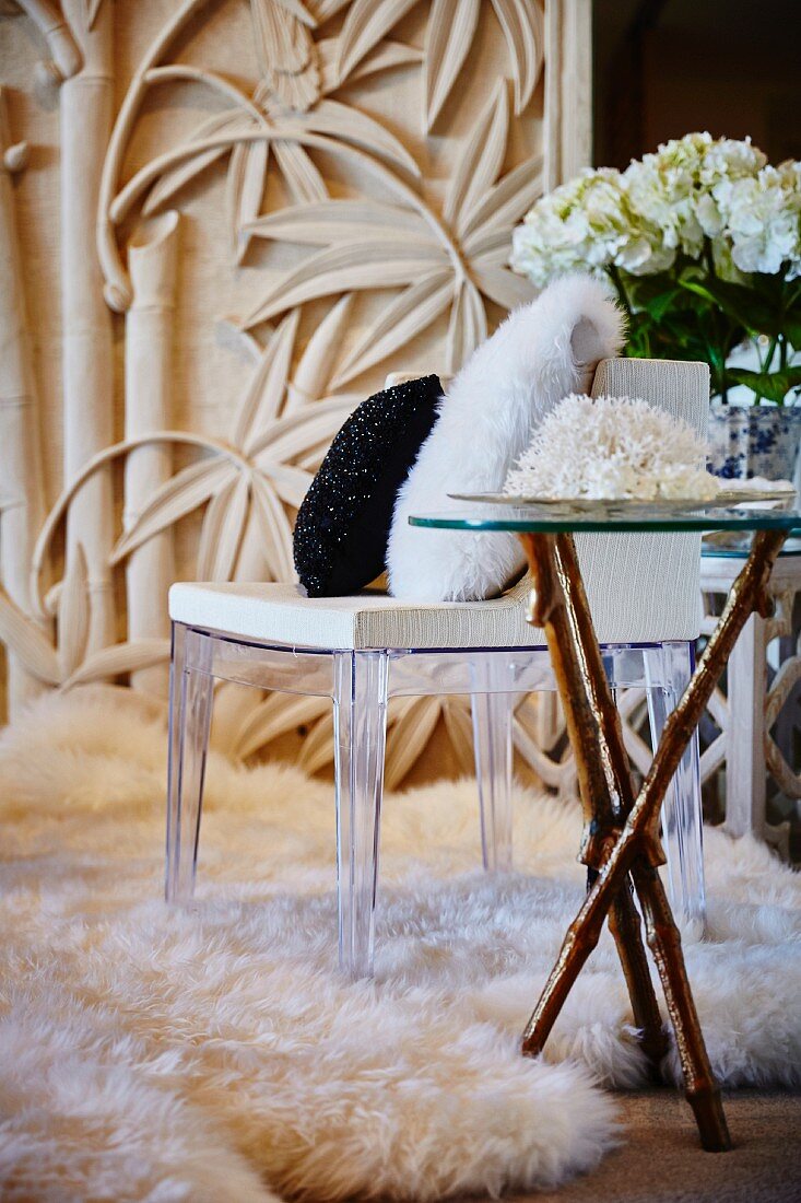 White coral on side table with wooden legs next to chair with plexiglas frame on flokati rug