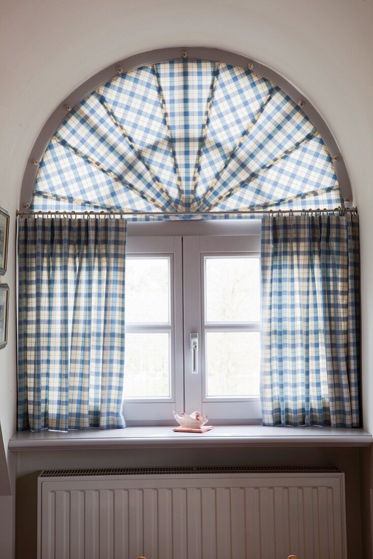 Rustic gingham curtains on window with semicircular transom in arched dormer window