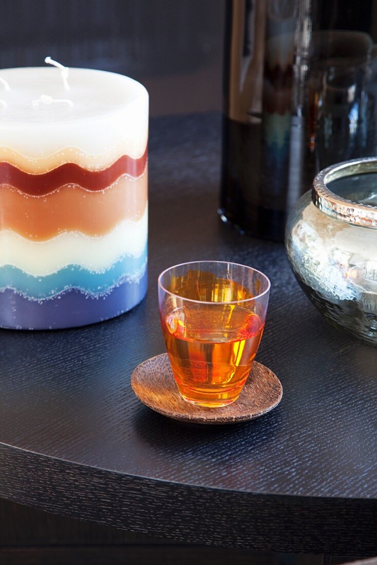 Orange gefärbtes Schnapsglas auf Holzuntersetzer neben einer Kerze