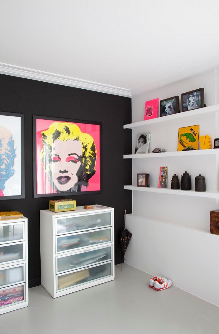 Prints of Marilyn Monroe on black wall above chests of drawers next to pictures and ornaments on white floating shelves