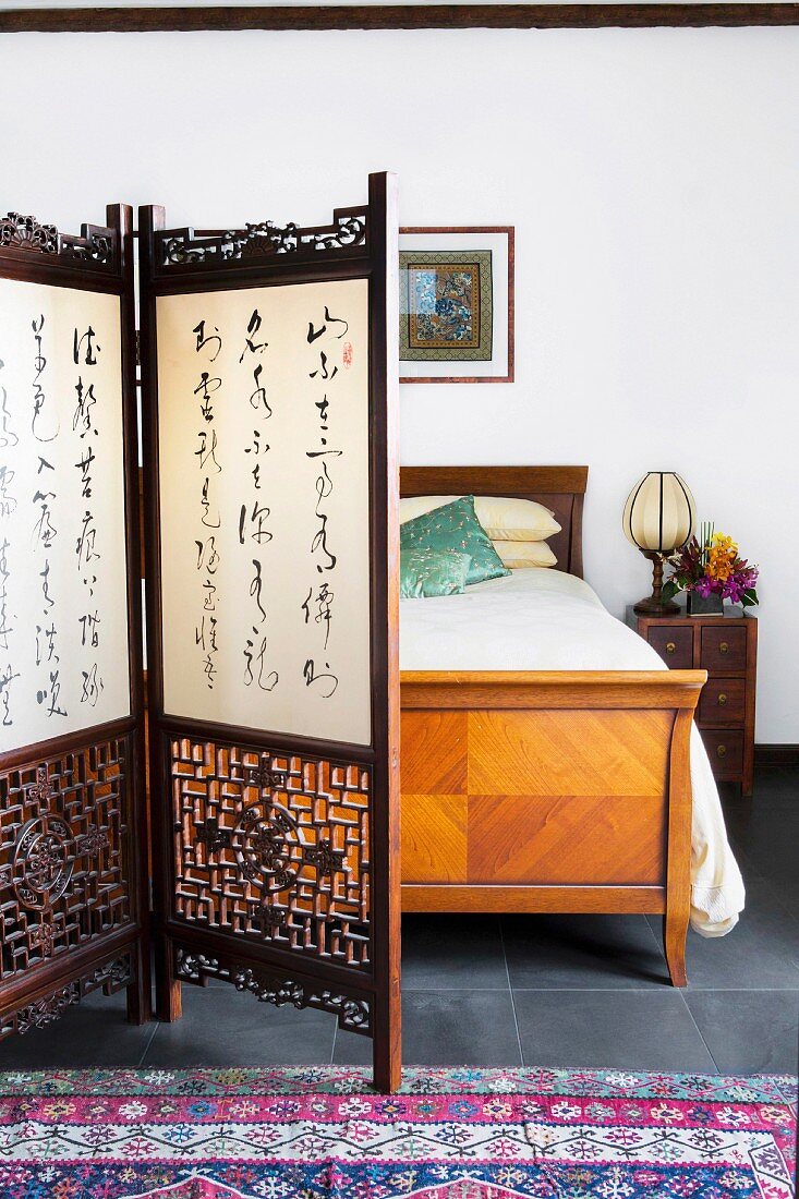 Geschnitzter Paravent mit asiatischen Schriftzeichen vor antikem Bett
