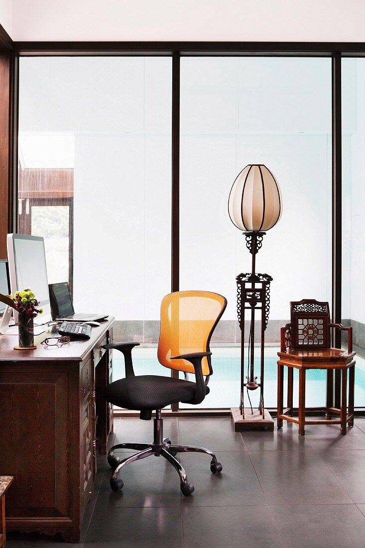 Desk with modern office chair, ethnic floor lamp in front of floor-to-ceiling glazing