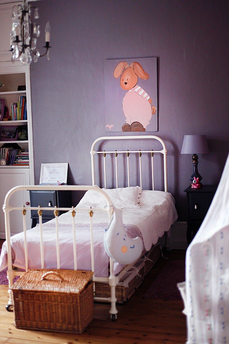 White metal bed below picture of rabbit on purple wall in vintage-style child's bedroom