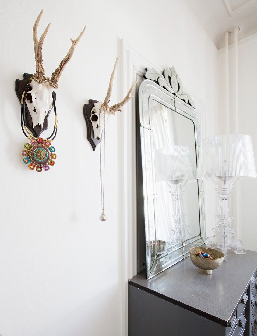 Hunting trophies used as jewellery racks next to chest of drawers with mirror on top