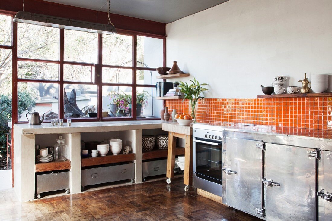 Offener Küchenbereich mit recyceltem Parkettboden, orangefarbenen Wandfliesen und Metallschränken
