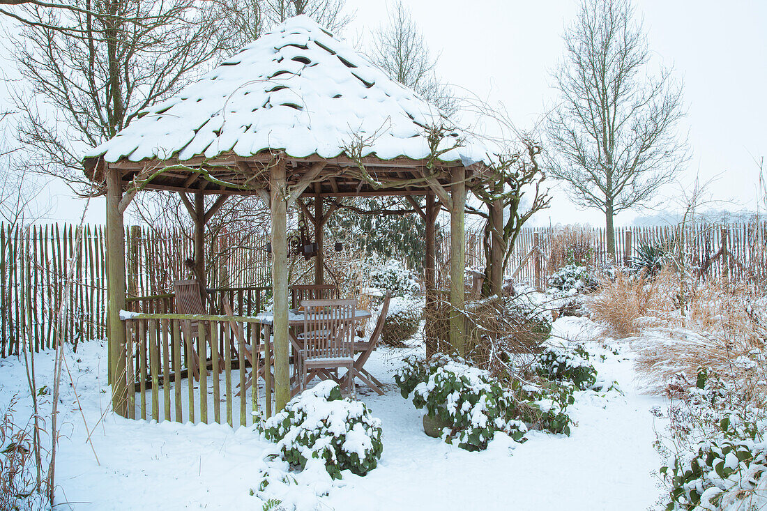 Holz-Pavillon mit schneebedecktem Dach im winterlichen Garten