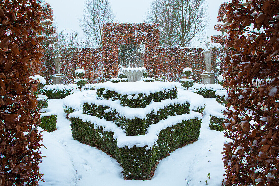 Symmetrischer Garten im Winter mit schneebedeckten Hecken und Bäumen