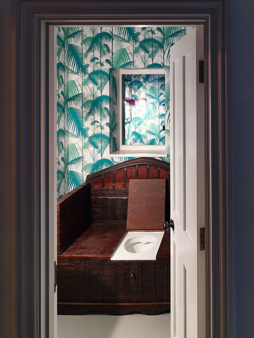 Blick in eine Toilette mit antikem Holz-WC und Dschungel-Tapete
