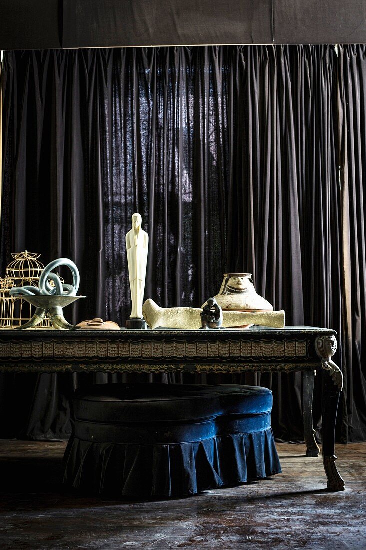 Sculpture on baroque table in front of dark curtain