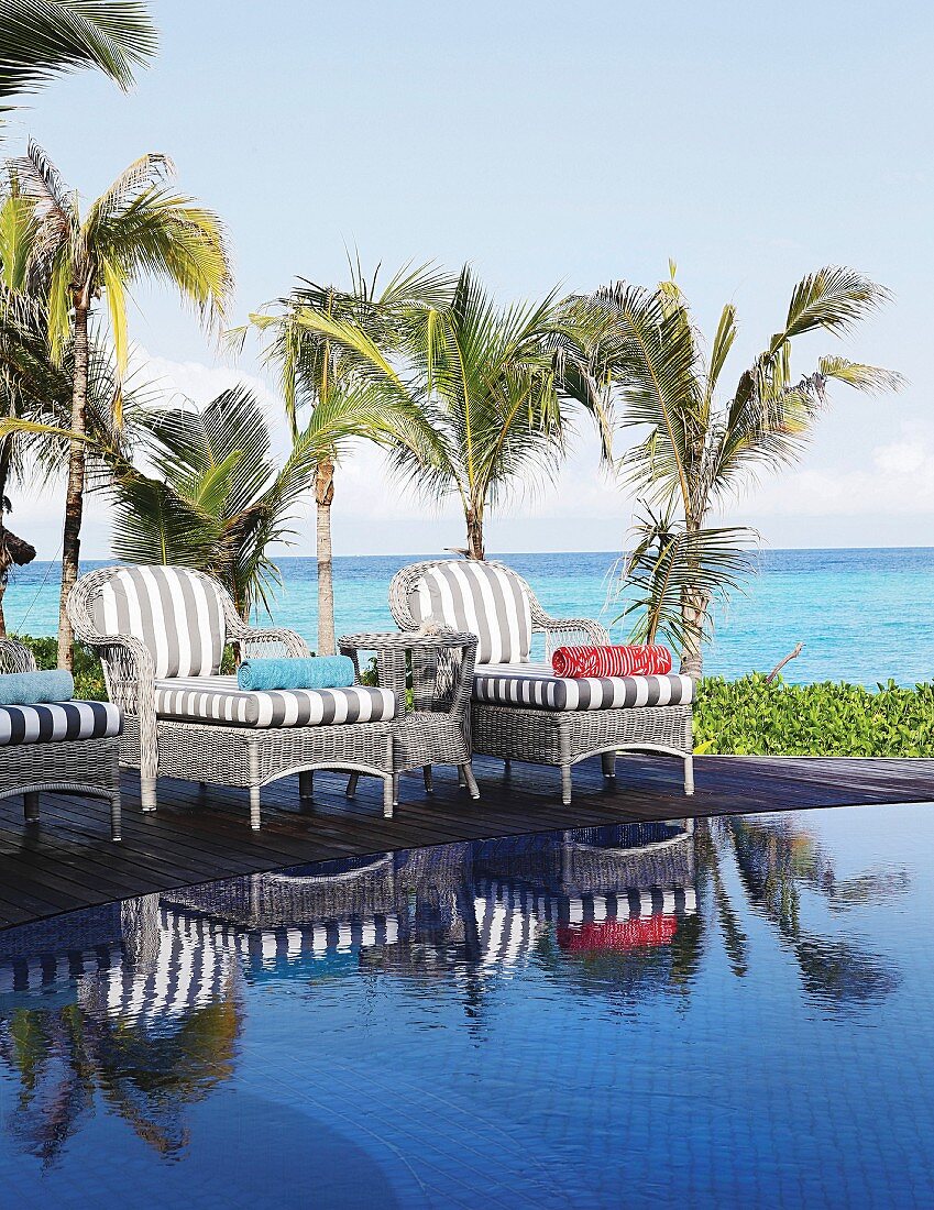 Wicker loungers with striped cushions next to pool with sea in background