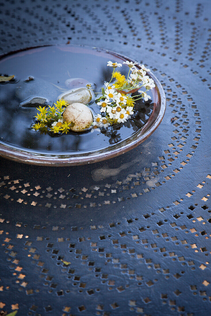 Bowl of water, pebbles and flowers on metal table