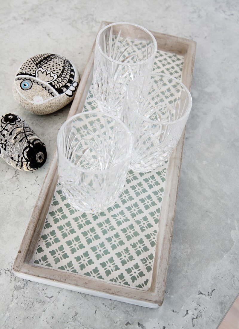 Three crystal glasses on patterned concrete tray next to painted pebbles