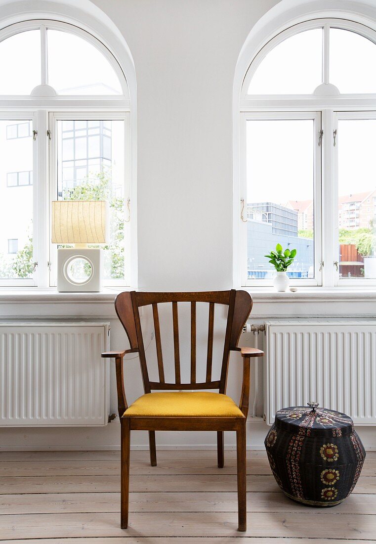Exotic-wood armchair next to ethnic wicker basket in front of arched windows in renovated period apartment