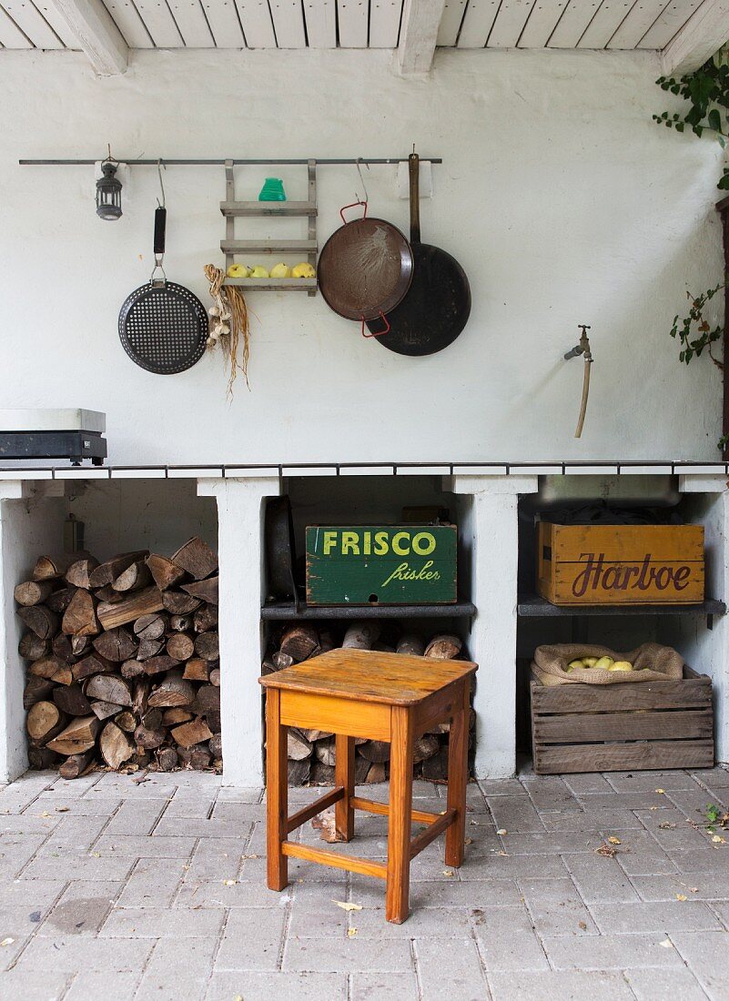 Rustikale Outdoor-Küche mit Brennholzlager, verschiedenen Holzkisten und aufgehängten Pfannen