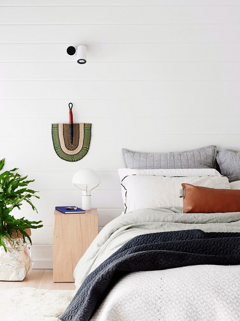 Helles Schlafzimmer mit weiß gestrichener Holzverschalung und Fächer als Wanddekoration
