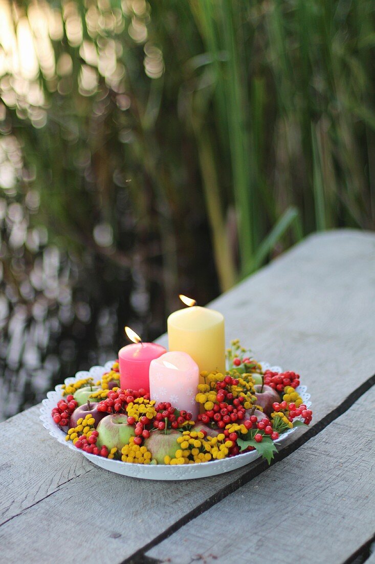 Autumnal arrangement of candles, berries, apples and flowers on outdoor table