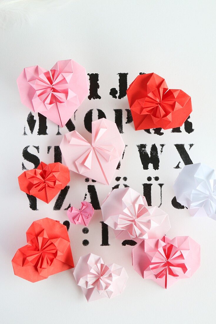 Origamiherzen in verschiedenen Rottönen auf Buchstaben-Druck