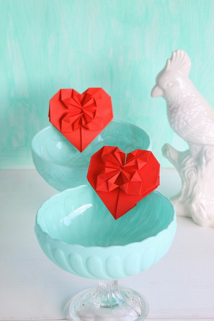 Red origami hearts in turquoise dessert bowls next to china bird