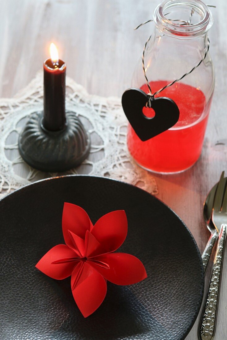 Red origami flower on black plate and red drink in bottle
