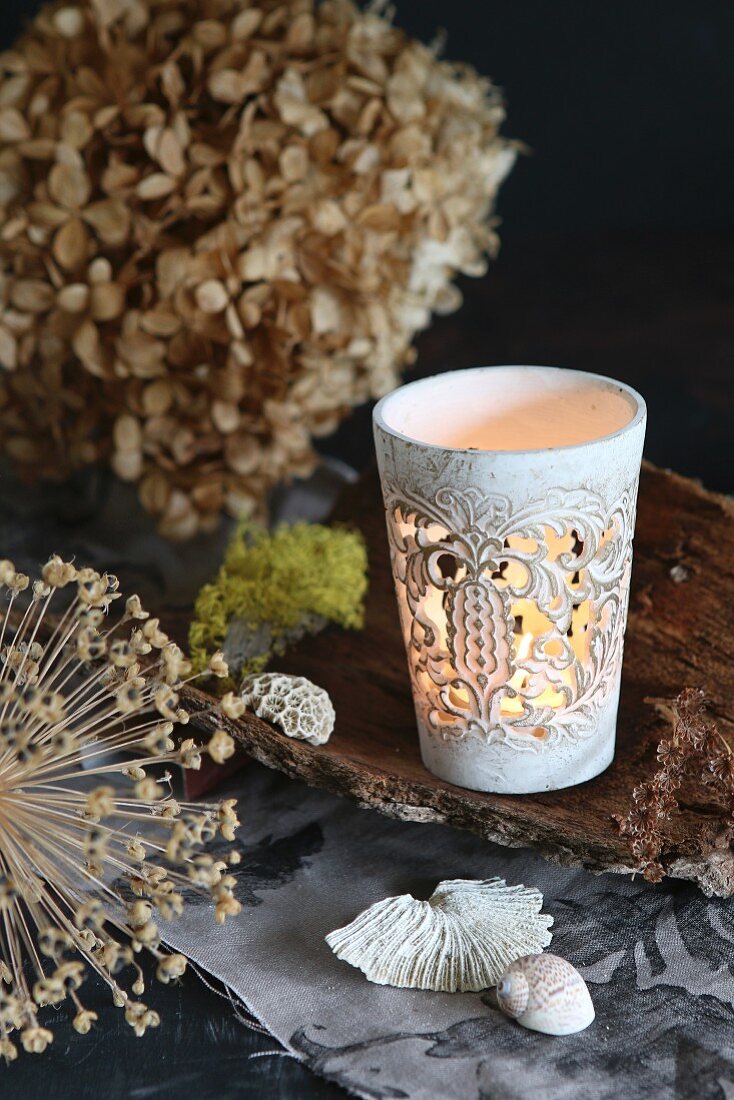 Ornate tealight holder on piece of bark next to dried flower heads