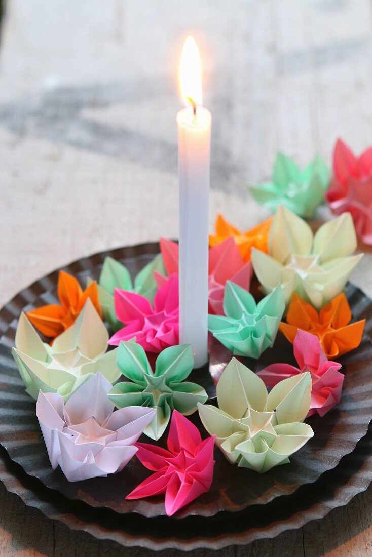 Bunte kleine Origami-Blumen auf schwarzen Tellern mit einer Kerze