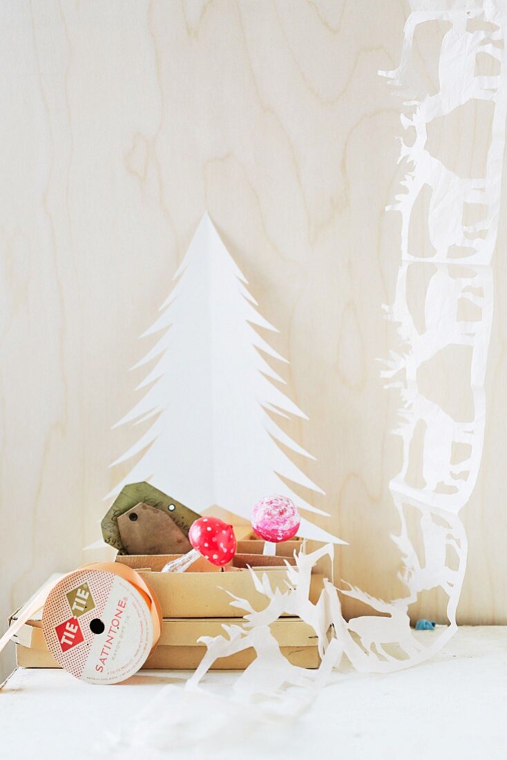 weiße DIY-Papiergirlande mit Hirschmotiven neben Papier-Tannenbaum und Pappschachteln mit Dekopilzen