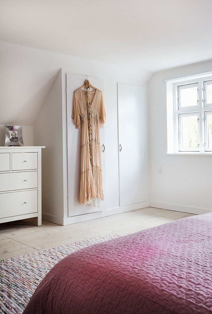 Dress hung on door of fitted wardrobe under sloping ceiling in bedroom