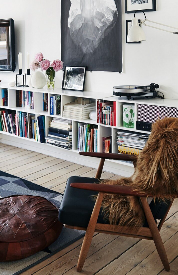 Brown fur blanket on retro armchair in front of books in sideboard