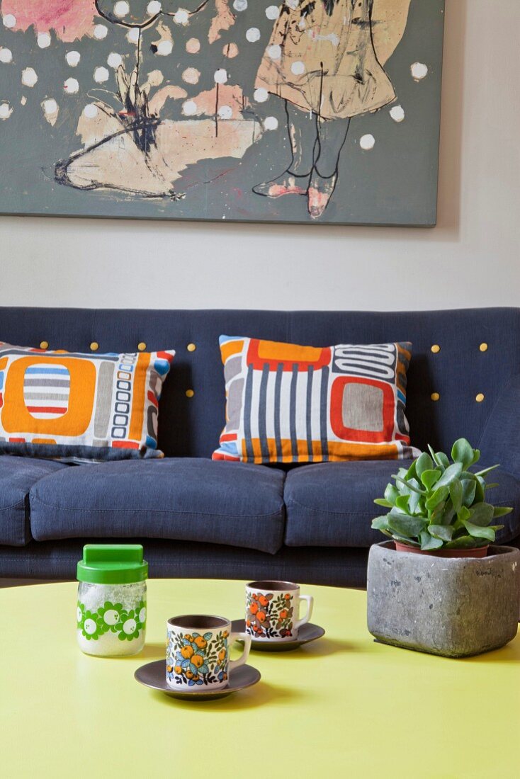 Retro cups on coffee table in front of patterned scatter cushions on sofa