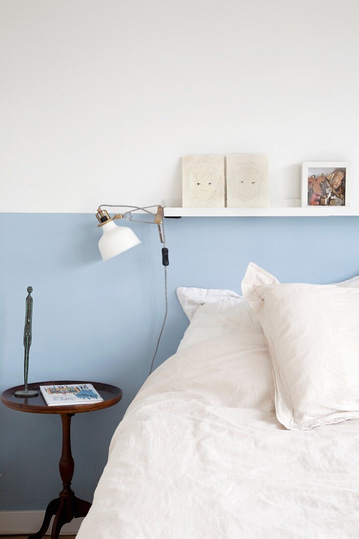 Bed below narrow shelf on wall with blue dado rail