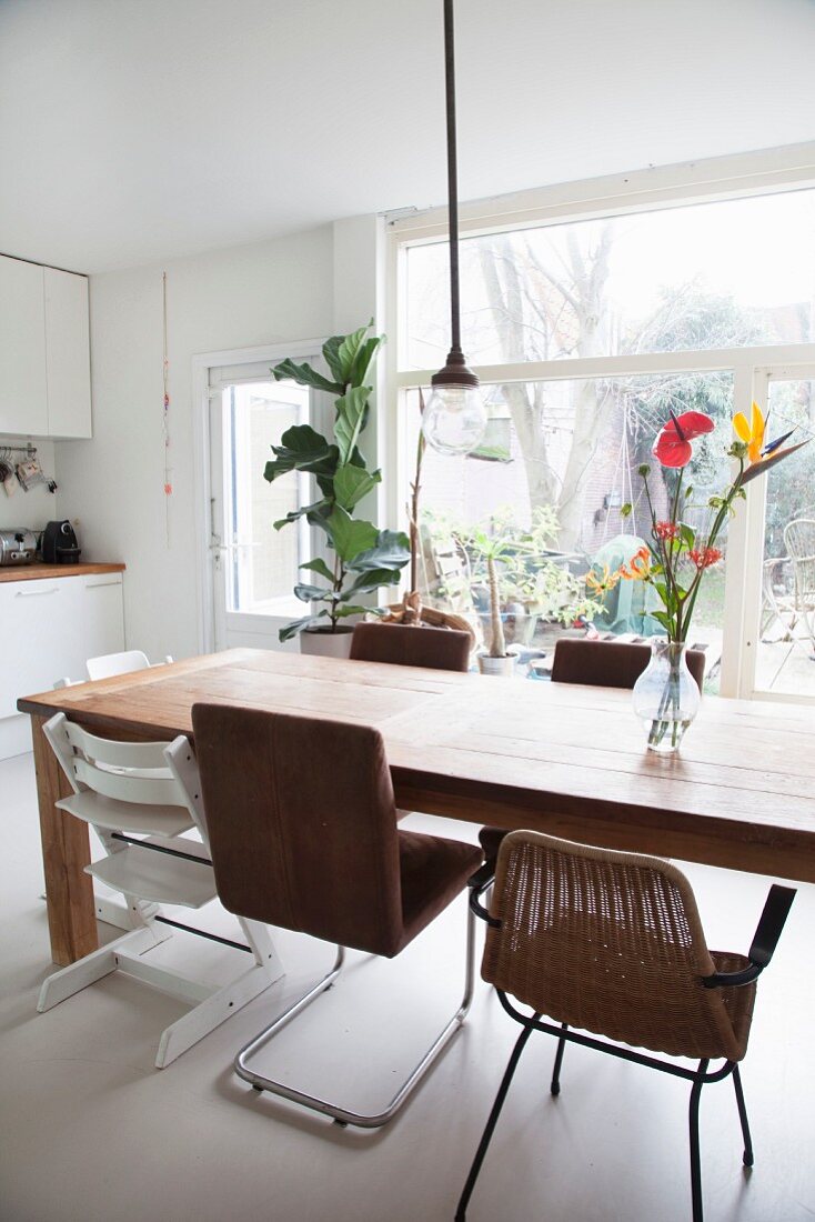 Esstisch mit verschiedenen Stühlen vor einer Fensterfront in der Küche