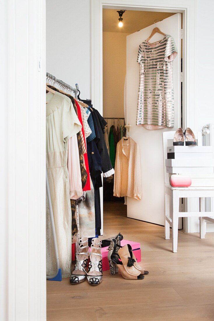 Women's clothing on clothing rail and hung on open door next to shoes and shoe boxes