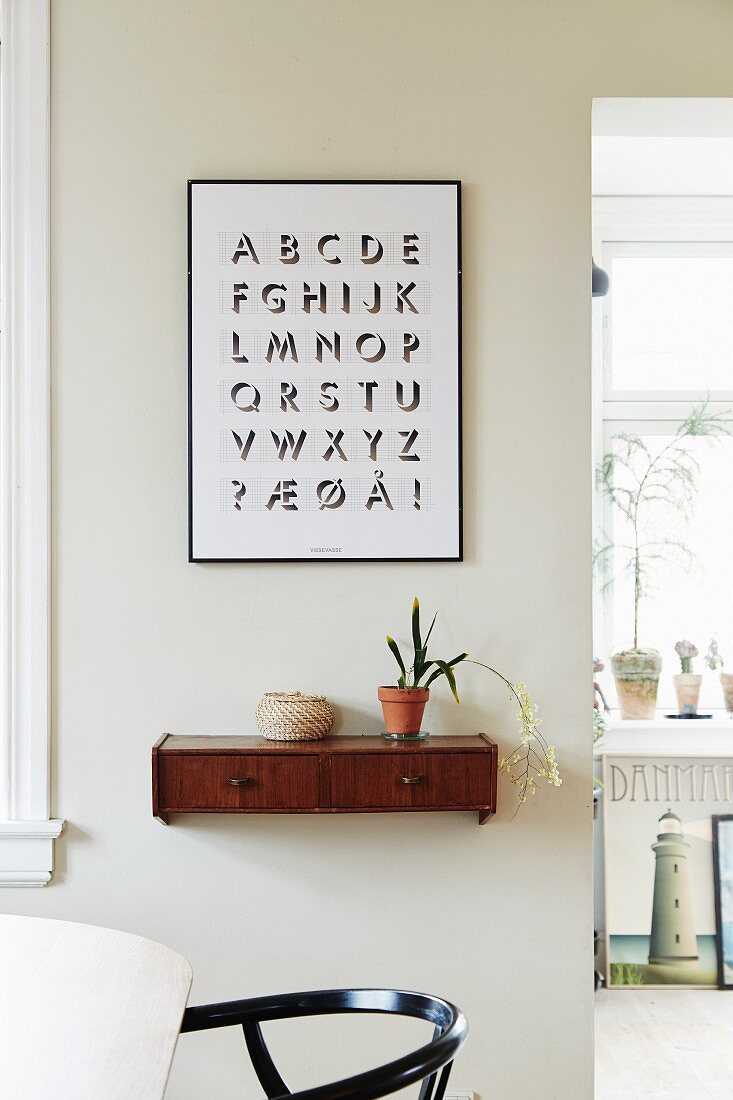 Graphic alphabet artwork above wooden wall-mounted shelf