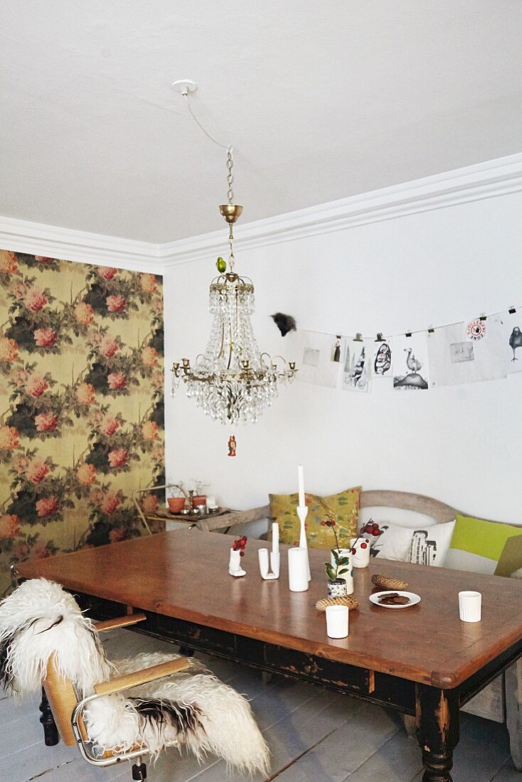 Vintage wooden table and crystal chandelier in front of accent wall with floral wallpaper