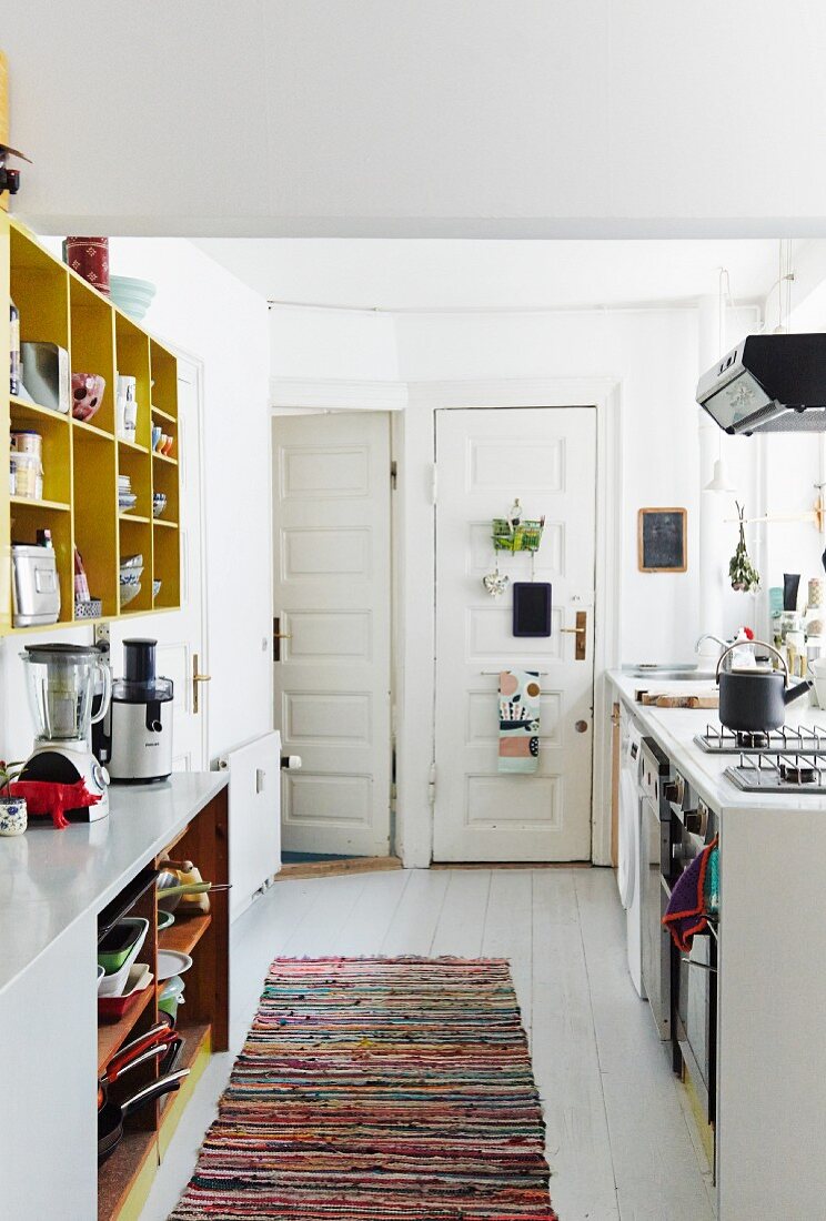 White-painted board floor, colourful rag rug and opposing kitchen counters in bright period apartment