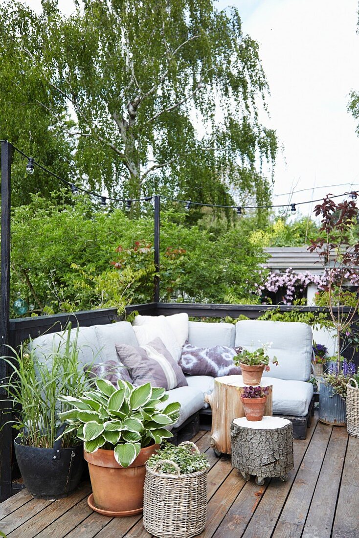 Paletten-Couch und rollbare Baumstamm-Hocker auf sommerlicher Terrasse