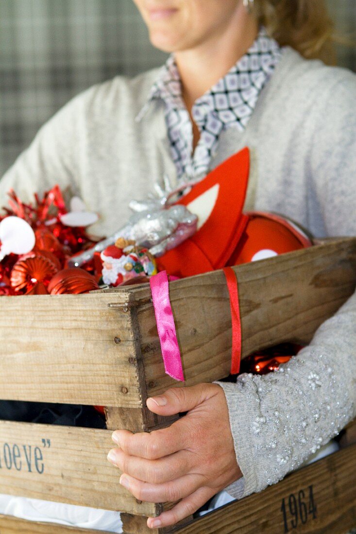 Frau trägt Holzkiste mit rotem Weihnachtsschmuck