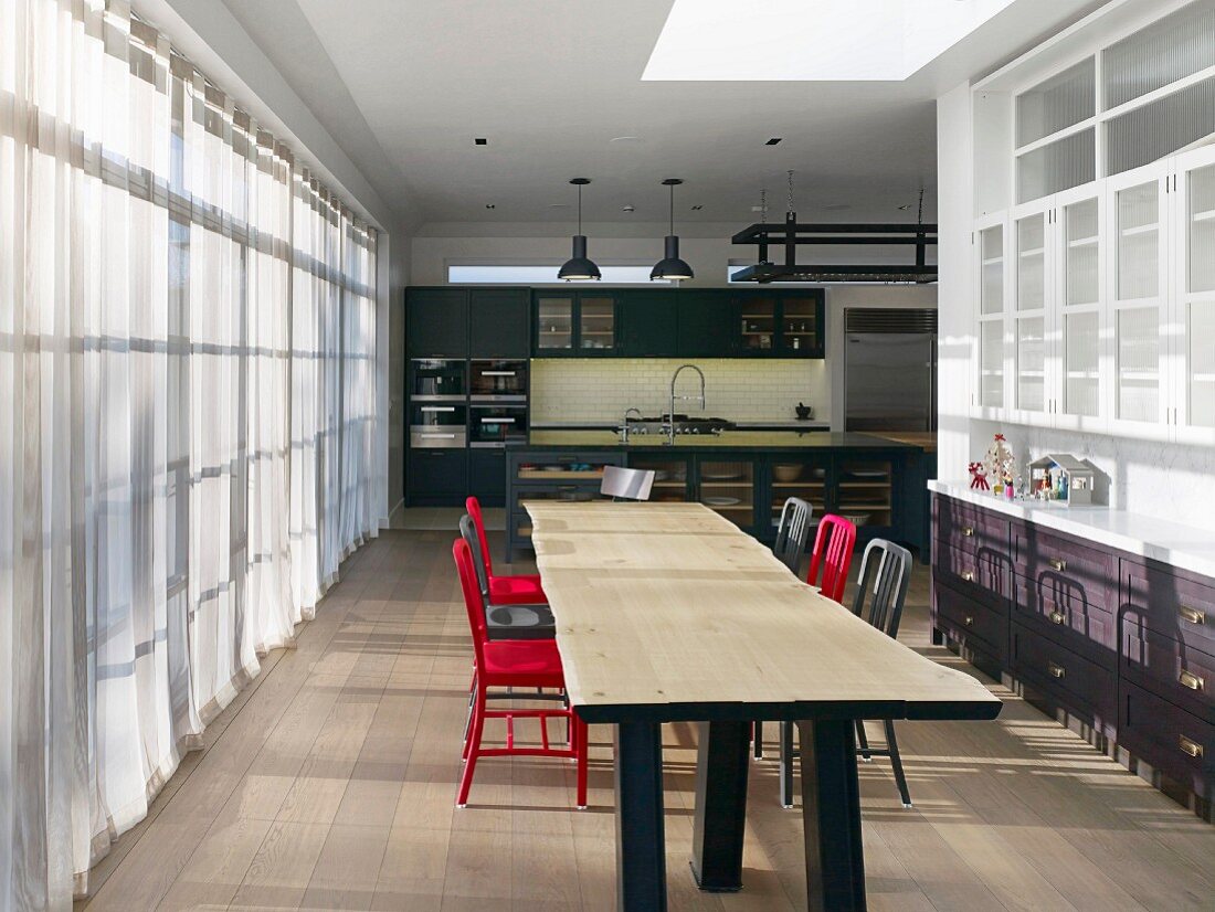 Blick über langen Esstisch aus Holz in die Küche im Industriestil